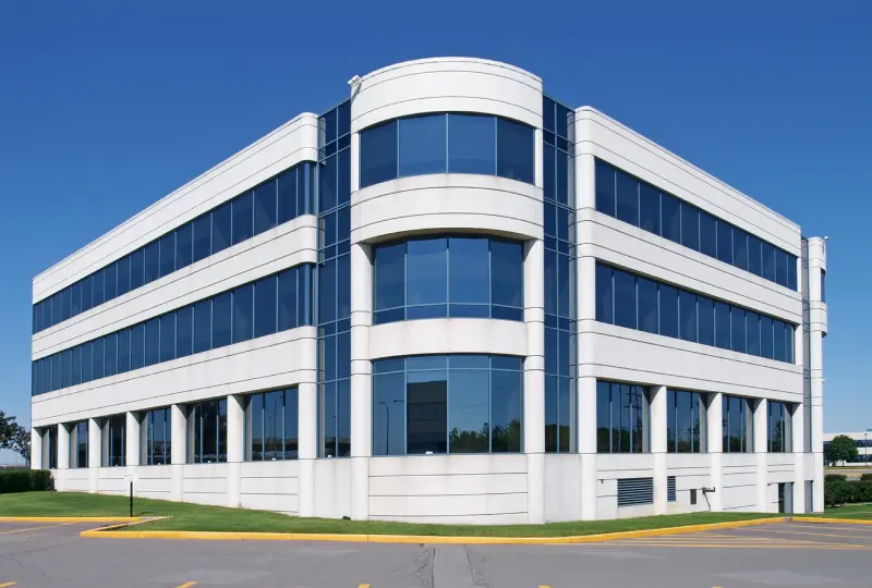 New Project (4) A modern three-story office building with large glass windows and a white facade, set against a clear blue sky.